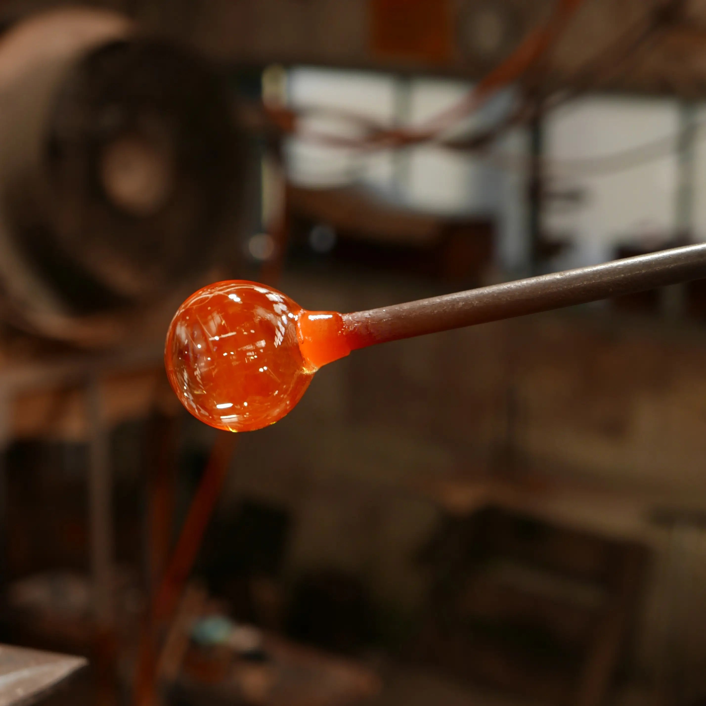 Molten glass on a rod with a blurred workshop background