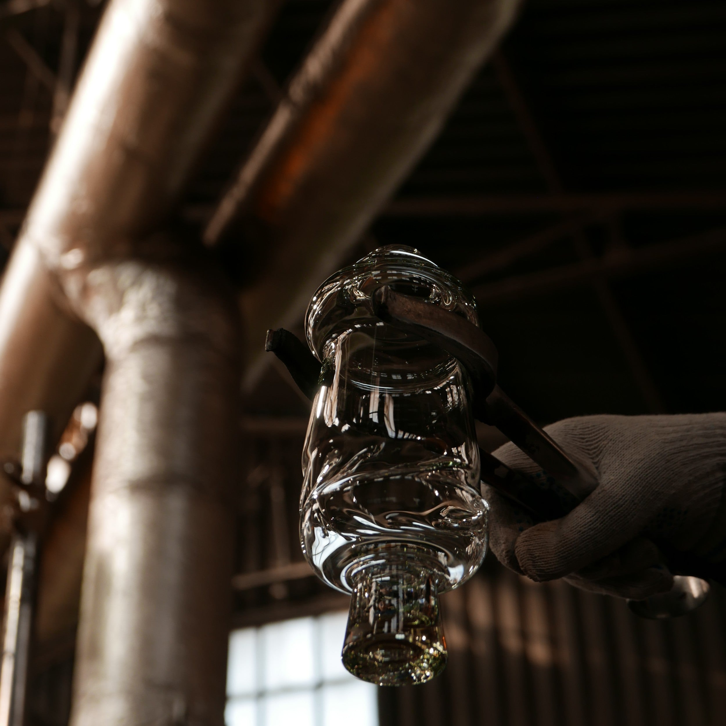 Hand holding a clear VIŚLA glass bottle with intricate design against an industrial background