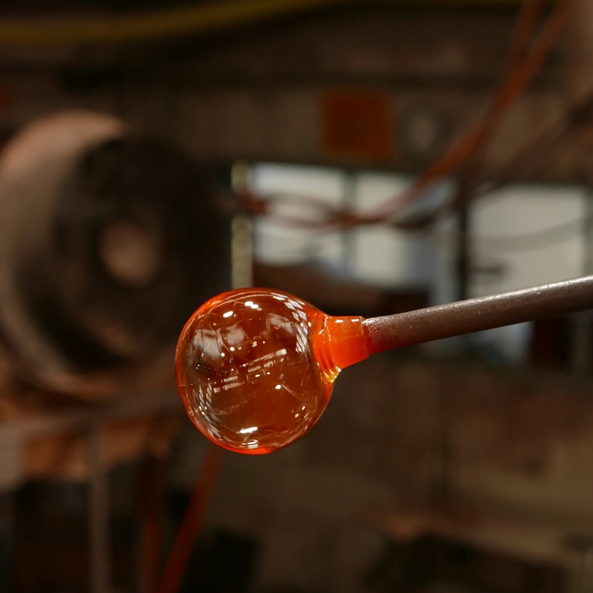 VISLA GLASSVERDE glassblowing process with molten glass on a rod against a blurred workshop background