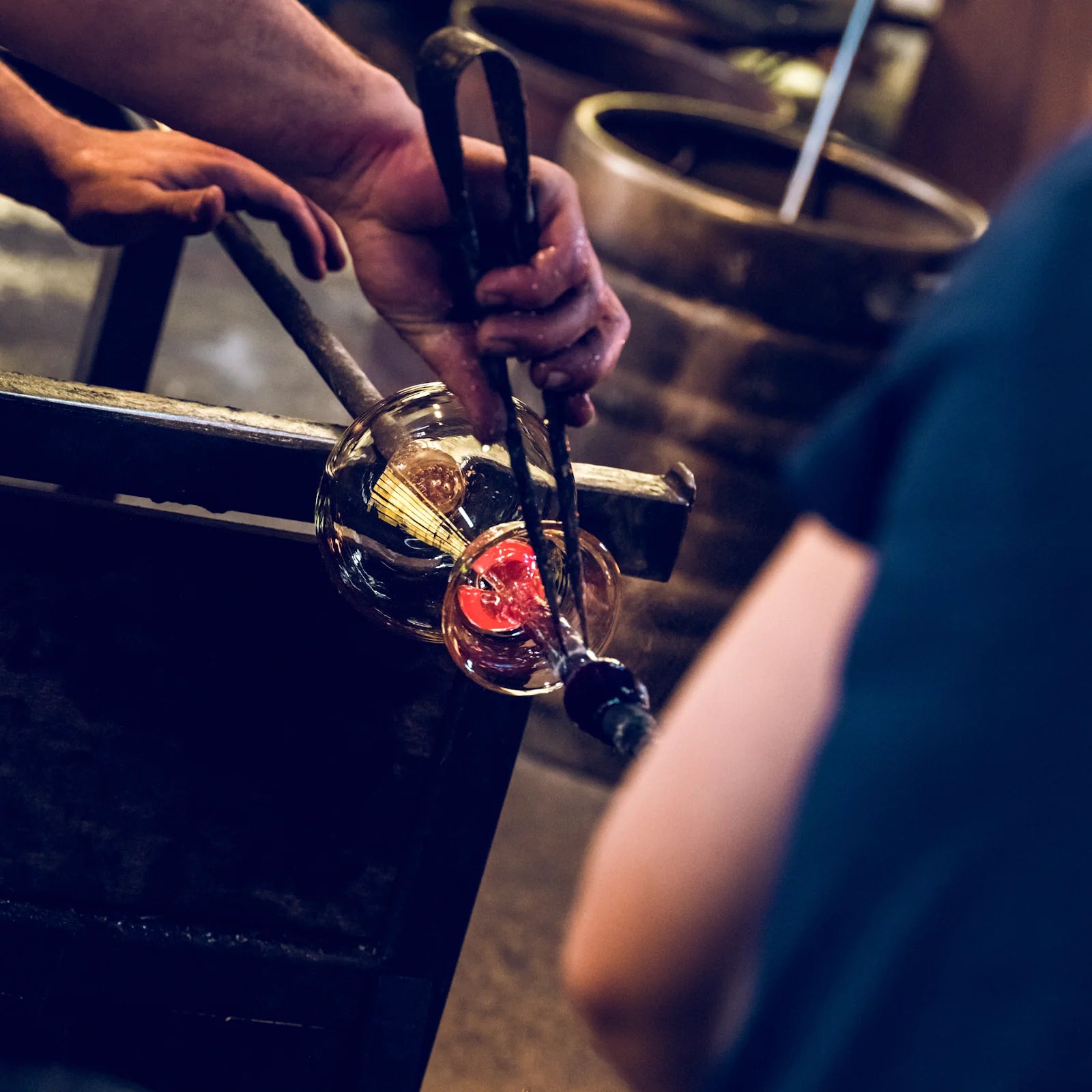 Glassblower shaping molten glass in a workshop setting
